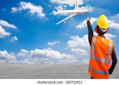 Rear View Of A Air Traffic Controller In Suit Pointing Airplane At The Runway Airport On Blue Sky Background