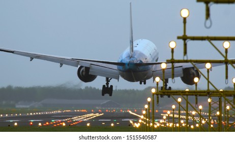 Rear view of aircraft landing at Schiphol airport at rainy weather. Shot from the beginning of runway. Landing lights at the foreground.