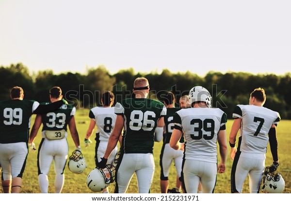 Rear view of an American\
football team walking on a playing field during a practice in the\
late afternoon