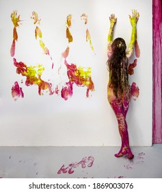 Rear view of an artistically painted young woman unrolling herself on the studio wall, leaving artistically colored imprints of her beautiful body, copy space.