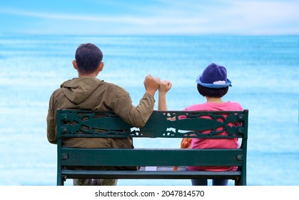 Rear view of Asian adult couple on metal bench showing pinky swear hand sign to be a relationship forever after Dating on the Beach, diverse people and love concept - Powered by Shutterstock