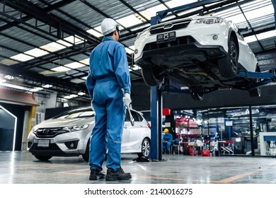 Rear view of Asian automotive mechanic repairman look under car condition in garage. Vehicle service male work in mechanics workshop, feel success after check andmaintenance to repair car engine car.