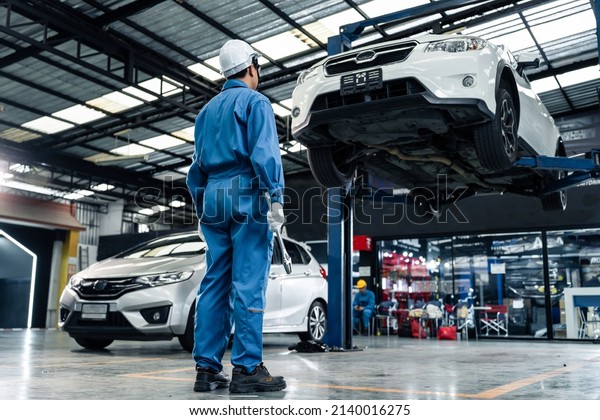 Rear view of Asian automotive mechanic\
repairman look under car condition in garage. Vehicle service male\
work in mechanics workshop, feel success after check andmaintenance\
to repair car engine car.