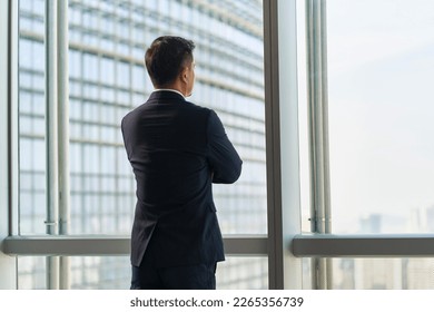 rear view of asian business man standing by the window looking at city view arms crossed - Powered by Shutterstock