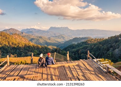 Rear view of asian couple enjoying the mountain view on wooden balcony in the evening at countryside. Hadubi viewpoint, Wiang Haeng, Chiang Mai, Thailand