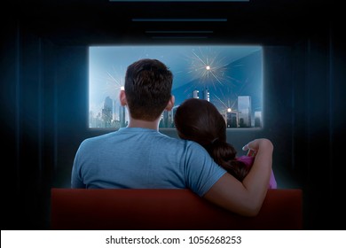 Rear View Of Asian Couple Watching Celebration On Tv At Dark Room