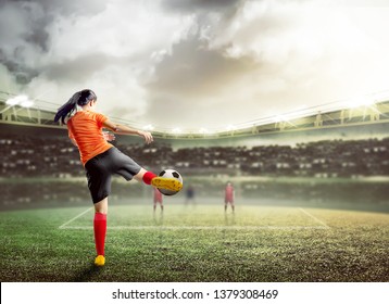 Rear View Of Asian Football Player Woman In Orange Jersey Kicking The Ball On The Football Field At Stadium