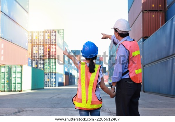 Rear view asian foreman father and his daughter\
holding hands while teaching little girl. Engineer dad with safety\
hat point something at container with kid at industrial container\
cargo freight ship