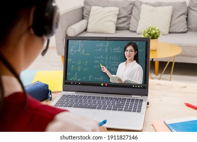 Rear View Of Asian Girl Is Learning Trigonometric Function Math Online With Female High School Teacher By Laptop At Home And Write Down The Note