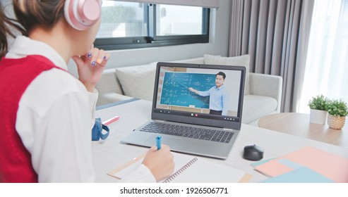 Rear View Of Asian Girl Is Learning Math Online Through Listening To Male High School Teacher Teaching Trigonometric Function By  Laptop At Home And Write Down The Note