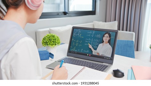 Rear View Of Asian Girl Is Learning Math Online Through Listening To Female High School Teacher Teaching Trigonometric Function By  Laptop At Home And Write Down The Note