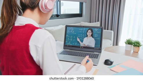 Rear View Of Asian Girl Is Learning Math Online Through Listening To Female High School Teacher Teaching Trigonometric Function By  Laptop At Home 