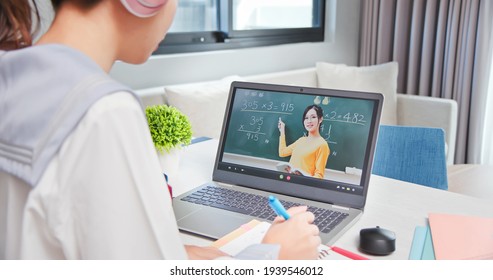 Rear View Of Asian Girl Is Learning Math And Looking Elementary School Female Teacher Teaching Online Through Laptop At Home