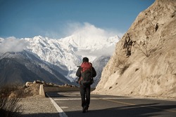 Rear View Of An Asian Hiker With Backpack Walking On Highway With Snowcapped Meili Mountain In Background
