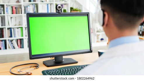 Rear View Of Asian Male Doctor Wear Headphone And Watch Computer Monitor With Green Screen 