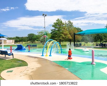 Rear View Asian Toddler Boy Playing At Splash Park Near Dallas, Texas, America. Colorful Recreation Site With Splashing Water Fountains For Kids Summertime Activities