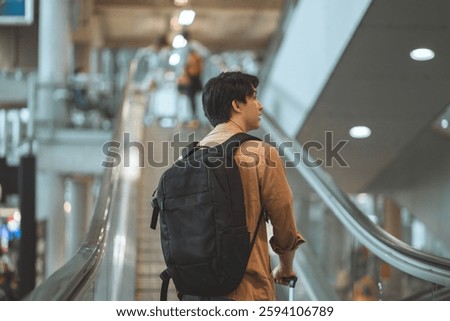 Rear view - Asian tourist man traveller with simple suitcase stand on moving walkway in airport terminal, Tourist journey trip concept