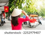 Rear view of Asian tourist woman is wearing Non La (traditional Vietnamese hat) and Ao Dai (traditional Vietnamese dress) enjoy sightseeing in Hanoi city Vietnam. Copy space