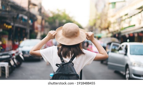 Rear View Of Asian Traveller Woman With Backpack And Hat Staycation Travelling At Outdoor On Day. Walking Street Market Background.