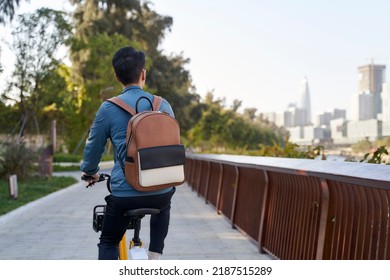 Rear View Of An Asian Young Adult Man Riding Bike In City Park