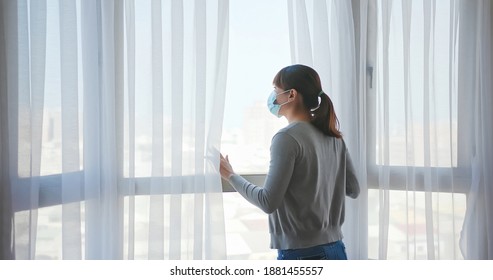 rear view asian young woman wearing face mask stay isolation at home for self quarantine due to epidemic of COVID19 - she looks out the window - Shutterstock ID 1881455557