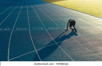 Rear View Of An Athlete Ready To Sprint On An All-weather Running Track. Runner Using A Starting Block To Start His Run On Race Track.