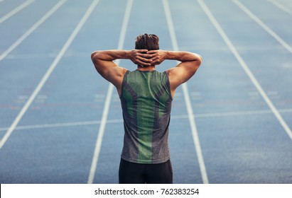 Rear View Of An Athlete Standing On A Running Track With Hands At The Back Of Head. Runner Getting Ready To Race Standing On Race Track.