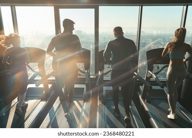 Rear view of athletic people running on treadmills in a gym with city view. Silhouettes of group of four people doing cardio in modern indoor environment.