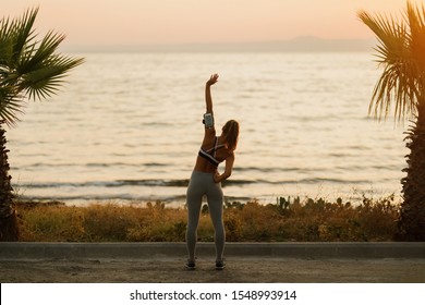 Rear View Of Athletic Woman Warming Up Before Sports Training By The Sea At Dawn. Copy Space. 