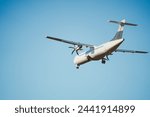 Rear view of an ATR 72 airplane in the clear blue sky. Twin-engine turboprop short-haul regional passenger aircraft. Landing airplane. Blue background.