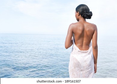 Rear view of an attractive african american black woman standing contemplating the sea on a holiday vacation trip during a summer day with a blue sea and sky. Health and beauty lifestyle and travel.