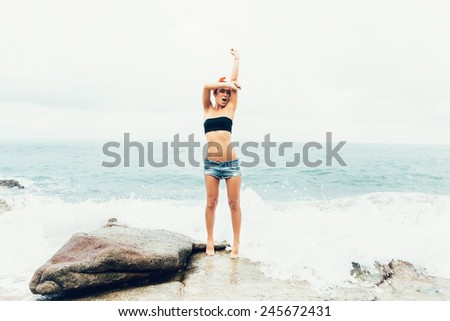 Rear view of an attractive woman having fun on a natural coastal rock high up, contemplating the sea against a blue sky. Well being healthy lifestyle