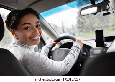 Rear view of attractive young woman in casual wear looking over her shoulder while driving car. Cheerful millennial confident, beautiful african american lady looks at passenger seat, copy space