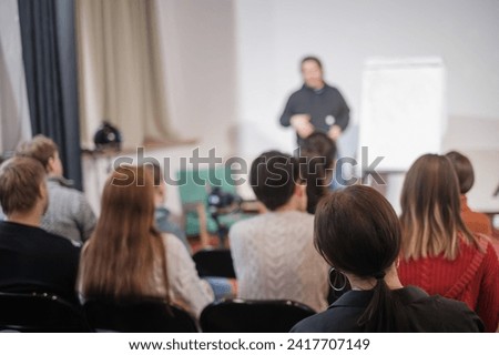 Rear view of an audience attentively listening to a blurred speaker during a professional business training session.