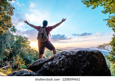 Rear view back of Young asian hiking man standing and rise-up hands with happy on peak of rocky mountain, copy space