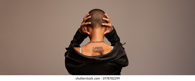 Rear View Of A Bald Woman Covering Her Ears On Grey Background. Woman With Shaved Head And Express Yourself Written On Her Back.