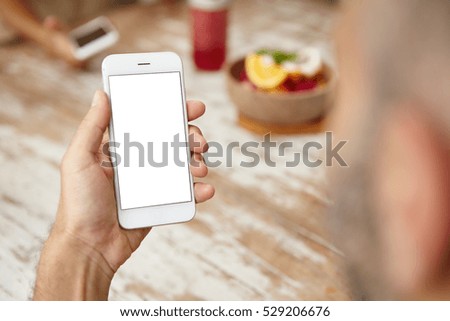 Rear view of bearded man checking e-mail or newsfeed on social networks, using free wireless internet connection at cafe. Male with smart phone in his hands messaging online. Selective focus
