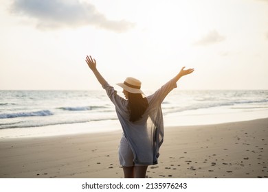 Rear view Beautiful asian woman stretching arm up into sky feeling happy at the beach with sunset. Take a break from work go on a trip. Woman travel in holiday weekend summertime. Relax vacation time