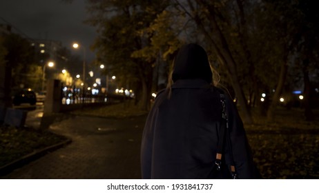 Rear view of a beautiful girl going through the park at night, she is frightened and begins to run. Action. Blond teenager girl looking scared at the city park late in the evening.
