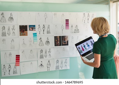 Rear view of beautiful mature Caucasian female fashion designer looking at sketch while holding laptop in design studio. Modern casual creative business concept - Powered by Shutterstock