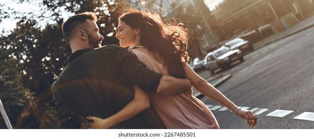 Rear view of beautiful young couple embracing and smiling while walking by the city street - Shutterstock ID 2267485501