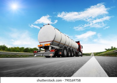 Rear view of big metal fuel tanker truck in motion shipping fuel on the countryside road against blue sky