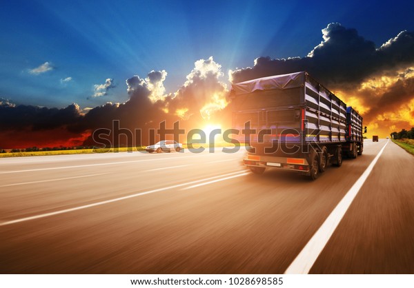 Rear view\
of the big truck driving fast with blue trailer on the countryside\
road against night sky with\
sunset