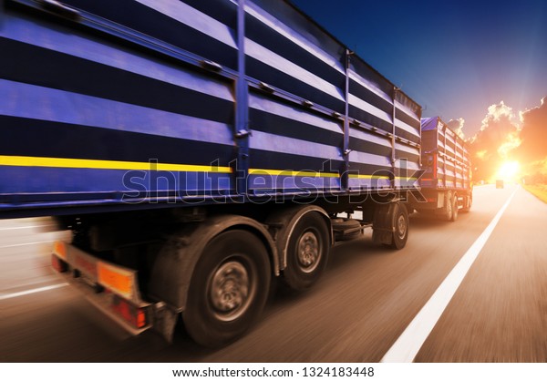 Rear view\
of the big truck driving fast with blue trailer on the countryside\
road against night sky with\
sunset