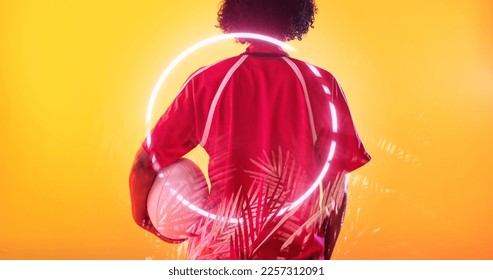 Rear view of biracial female rugby player with ball standing over illuminated circle and plants. Copy space, composite, sport, competition, shape, nature, playing, match and abstract concept. - Powered by Shutterstock