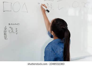 Rear view of biracial schoolgirl writing on whiteboard in class, with copy space. Education, childhood, elementary school, inclusivity and learning concept. - Powered by Shutterstock