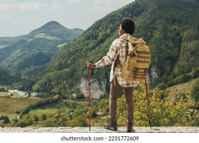 Rear view of a black woman with backpack and trekking poles standing in nature and enjoying in fresh air while hiking on mountain. - Powered by Shutterstock