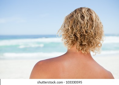 Rear view of a blonde man standing in front of the ocean - Powered by Shutterstock