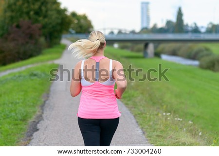 Rear view of blonde woman wearing sportswear running along river in a close up view