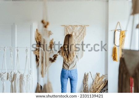 Rear view of blonde woman weaving macrame in a home workshop. Female knits weaving macrame pinned on a wooden stick. Women hobby.
